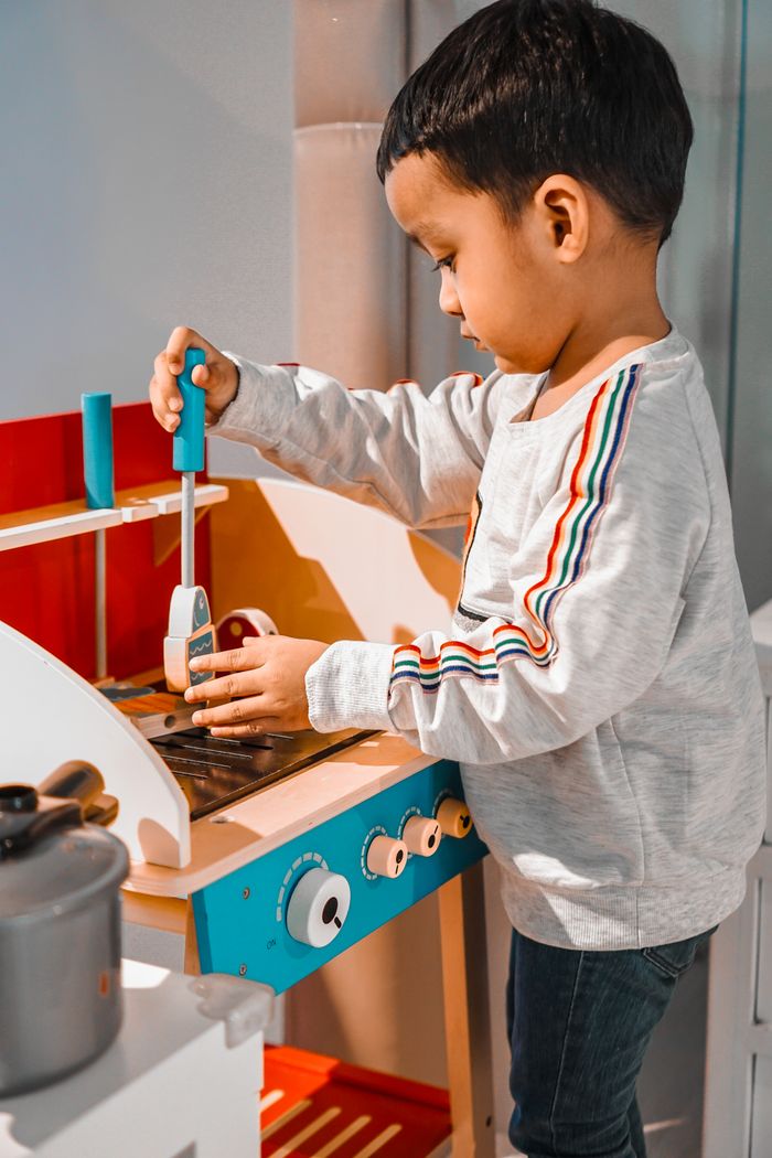 Adorable child engaged in fun playtime with a miniature kitchen toy indoors.